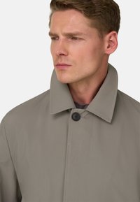 Trench coat grigio chiaro con colletto alto, chiusura con un solo bottone nero, tessuto liscio e vestibilità su misura. Caratterizzato da linee pulite e un design minimalista.