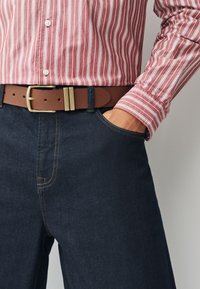 Red and white striped long-sleeve shirt worn with dark denim jeans. A brown leather belt featuring a brass buckle secures the outfit.