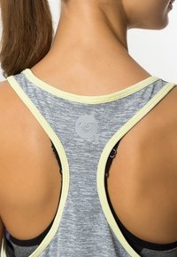 Szary sportowy top na ramiączkach z pleczeniem typu racerback, z jasnżółtym wykończeniem i okrągłym szarym logo z tyłu.