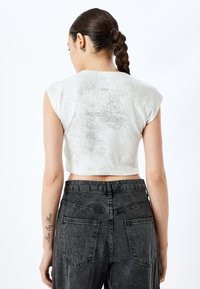 Vitt kortärmat topp med korta ärmar, lätt glans och texturerat utseende, kombinerat med högmidjade svarta denimjeans med bakfickor.