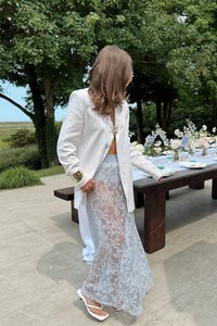 Bela lanena blazer z okrasnim gumbom, v kombinaciji s prosojno čipkastno maksi krilo v svetlo modri barvi. Preprostimi belimi sandali dopolnjujemo videz.