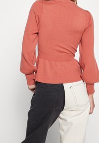Haut en tricot côtelé pêche avec des manches bouffantes, taille cintrée et ourlet évasé. Associé à un pantalon taille haute, un côté noir et l'autre blanc.