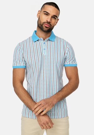 Kortærmet polo shirt i lyseblå med et geometrisk mønster i rød og blå. Har en ensfarvet blå krave og matchende manchetter. Lavet af en bomuldsblanding.