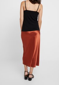 Camisola nera con spalline sottili abbinata a una lunga gonna di satin color ruggine. La gonna ha una texture liscia e un design lungo fino al pavimento.