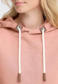 Haut à capuche rose avec un cordon de serrage, présentant une texture douce et des accents en cuir marron au niveau des œillets. Gros plan de la zone du cou.