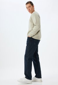 Sudadera gris claro con textura acanalada, vaqueros de denim azules y zapatillas blancas. Enfocado en un ajuste casual y detalles de diseño sencillos.