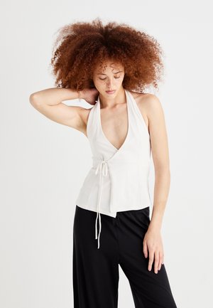 White halter top with a deep V-neck, adjustable tie at the waist, and a fitted bodice. Smooth texture. Paired with black loose-fit pants.