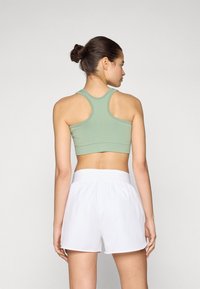 Soutien-gorge de sport vert avec un design dos nageur. Associé à des shorts blancs à taille élastique. Le matériau semble lisse et extensible.