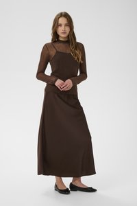 Dlhá hnedá sukňa v kombinácii s priliehavým hnedým textúrovaným topom. Oblečenie má hladký vzhľad a dopĺňajú ho čierne baleríny.