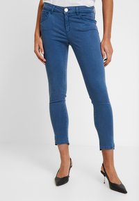 Blå smala jeans gjort av denim, med framfickor, dragkedja och en kort längd med en lätt frans vid fållen.