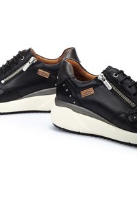 Zapatillas de cuero negro con acentos grises, que presentan un acabado texturizado, cremalleras laterales, una suela blanca gruesa y tachuelas plateadas en el talón.