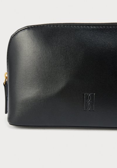 Μαύρη δερμάτινη θήκη με λεία υφή, στρογγυλεμένες άκρες, χρυσλό φερμουάρ και ανάγλυφο λογότυπο στην μπροστινή πλευρά. Συμπαγής και απλός σχεδιασμός.