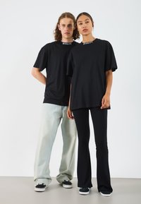 Två personer har på sig stora svarta T-shirts med ribbad krage. En har ljusblå jeans, medan den andra har svarta utsvängda byxor och sneakers.