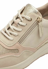 Baskets beiges avec tissu texturé, accents en cuir et quincaillerie dorée. Comprend des lacets, une fermeture éclair latérale et des détails cousus.