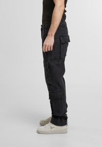 Pantaloni cargo negri dintr-un material durabil, cu buzunare laterale, o croială lejeră și asortați cu adidași albi pentru un aspect casual.