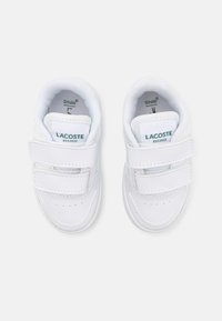 Fehér, szintetikus anyagból készült sportcipők, két tépőzárral, perforált orrdesignt kapott, zöld Lacoste logóval a nyelvén.