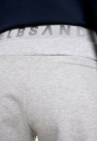 Graue Jogginghose mit einem strukturierten Bund und einem dezenten aufgedruckten Logo. Der Stoff wirkt weich und lässig, für Komfort entworfen.