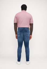 Kortärmad polotröja i ljusrosa med vita accenter, kombinerad med åtsittande blå jeans och vita sneakers. Fokusera på baksidan.