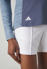 Blue striped long-sleeve top with a dark blue panel and white Adidas logo, paired with white shorts. Focus on texture and color contrast.