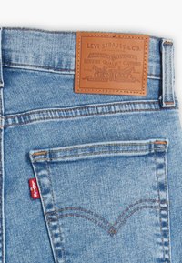 Svijetloplavi traperice s kožnom etiketom na kojoj piše "Levi Strauss & Co." i crvenom oznakom na stražnjem džepu. Uključeni su klasični detalji šivanja.
