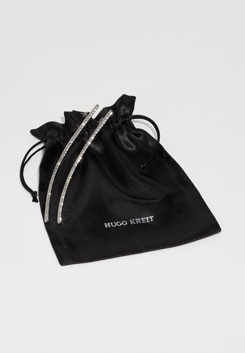 Black satin drawstring pouch with "HUGO KREIT" logo. Features two silver decorative bars with clear embellishments on top.