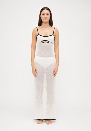 White mesh dress with open cut-out at chest, thin black straps, fitted bodice, and a flowing silhouette, featuring a contrasting black hem.