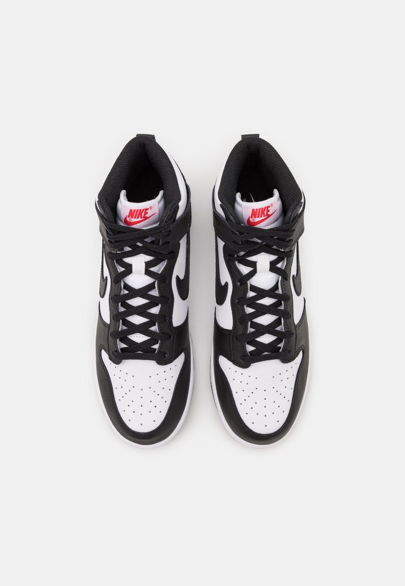 Zapatillas altas en blanco y negro con una parte superior de cuero y malla, puntera redonda, caja de puntera blanca perforada y logo de Nike rojo en las lengüetas.