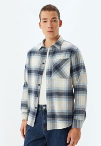 Camisa de franela con un patrón a cuadros en azul y crema, cierre de botones, un bolsillo en el pecho y textura suave con mangas largas.