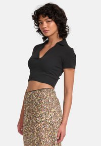 Polo-shirt noir cropped avec un col en V, associé à une jupe à imprimé floral coloré dotée d'une taille ajustée.