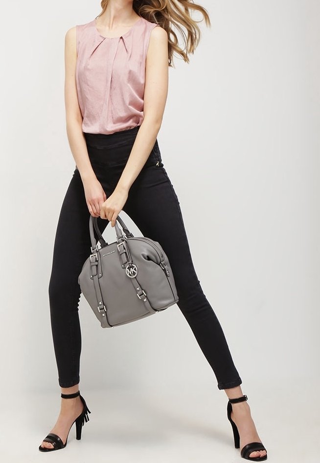 Bolso gris con herrajes plateados, forma redondeada y dos asas superiores. Combinado con una blusa sin mangas de color rosa claro y jeans ajustados negros.