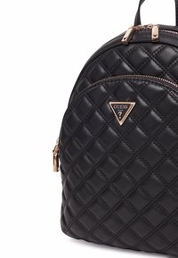 Zaino trapuntato nero con hardware dorato e logo triangolare. Presenta tasche con zip e una finitura liscia.