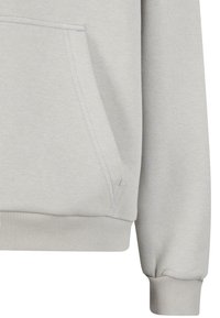 Manche et poche avant de sweat-shirt gris clair avec poignets et bas côtelés, montrant des coutures détaillées sur un tissu doux.