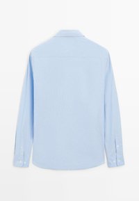 Chemise à manches longues bleu clair avec une texture douce, des poignets boutonnés et un col classique avec un ourlet arrondi. Vue de dos affichée.