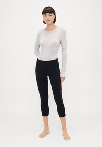 Maglietta grigia chiara a maniche lunghe con scollatura rotonda, abbinata a leggings neri attillati, tagliati sotto il polpaccio, con un discreto dettaglio del logo.