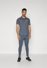 Grå atletisk polo og buksesæt med røde accenter, logo på brystet, korte ærmer og slim fit design; parret med sorte sportsko.