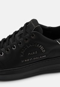 Černé tenisky s černými tkaničkami, reliéfní text "KARL LAGERFELD PARIS 21 RUE ST-GUILLAUME" na boku a detail na jazyku s logem.