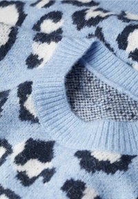 Gros plan d’un pull bleu doux avec imprimé léopard noir et blanc et col rond côtelé.