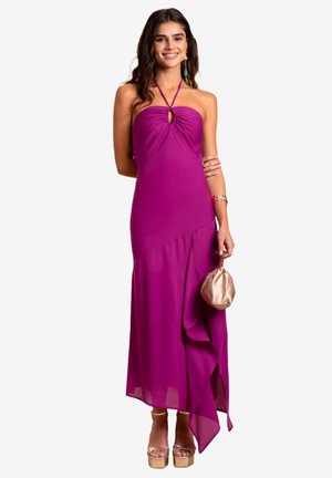 Lila Abendkleid mit Halterneck, Schlüssel-Ausschnitt vorne, fließendem Saum und Rüschen. Kombiniert mit einer beigen Clutch und silbernen Absätzen.