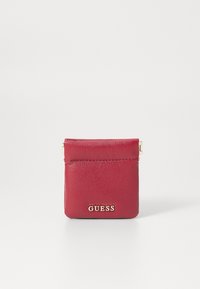 Portamonete in pelle rossa con una texture liscia, caratterizzato da un logo "GUESS" in tonalità oro e una chiusura superiore sicura. Forma compatta e rettangolare.