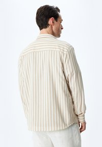 Camisa a rayas beige con una textura suave, que presenta mangas largas, un cuello clásico y detalles de botones en los puños y el yugo trasero.