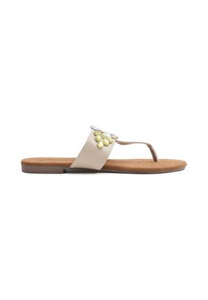 Sandalia plana de tiras en beige con una suave plantilla de ante marrón. Presenta gemas decorativas en azul y amarillo en la tira.