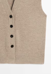 Beżowa dzianinowa kamizelka z dekoltem w serek, wyposażona w sześć czarnych guzików z przodu oraz prążkowany dół. Miękka w dotyku, bez rękawów.