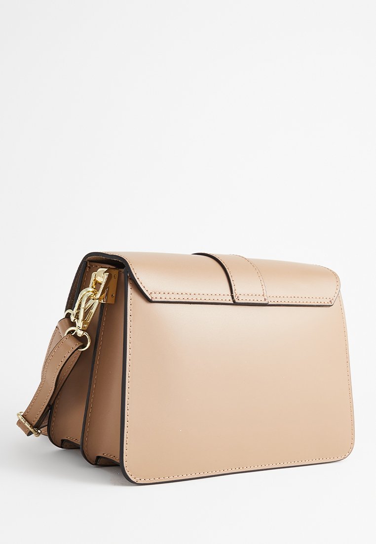 Beżowa skórzana torebka o mocno zarysowanym, prostokątnym kształcie, z klapą i zapięciem w złotym kolorze, na odpinanym pasku na ramię.
