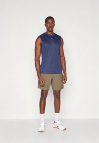 Marineblauw mouwloos sportshirt gecombineerd met kaki korte broek. De outfit bestaat uit een lichtgewicht, ademende stof en minimale logodetails.