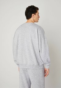 Sweatshirt grigio oversize in morbido tessuto, con scollatura rotonda e polsini a coste, dal taglio rilassato e spalle scese.