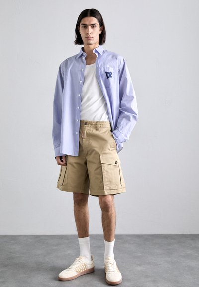 Light blue and white striped button-up shirt, beige cargo shorts, white socks, and cream sneakers with brown accents. Simple, casual ensemble.