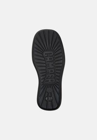 Suela de zapato de goma negra con un patrón radial y el logo "CAMPER" en el centro, diseñada para ofrecer agarre y durabilidad.