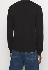 Svart långärmad t-shirt med texturerad yta och rund halsringning, bärs med blå jeans som har bakfickor och en lös passform.