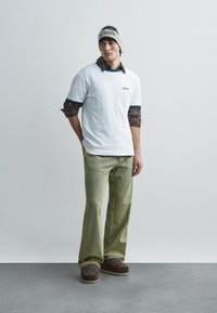 Balti marškinėliai trumpomis rankovėmis, dėvimi ant languotos ilgomis rankovėmis marškinio, derinami su šviesiai žaliais dryžuotais kelnėmis ir rudais slip-on batais. Pilka vilnonė kepurė.