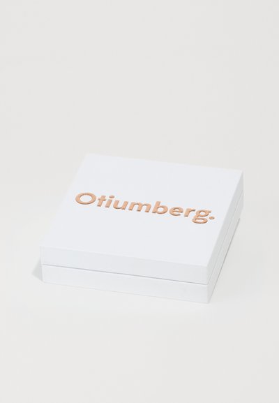 Weißer rechteckiger Kasten mit glatter Oberfläche, verziert mit erhabenen roségoldenen Buchstaben, die "Otiumberg" lesen. Kompaktes Design mit klaren Linien.